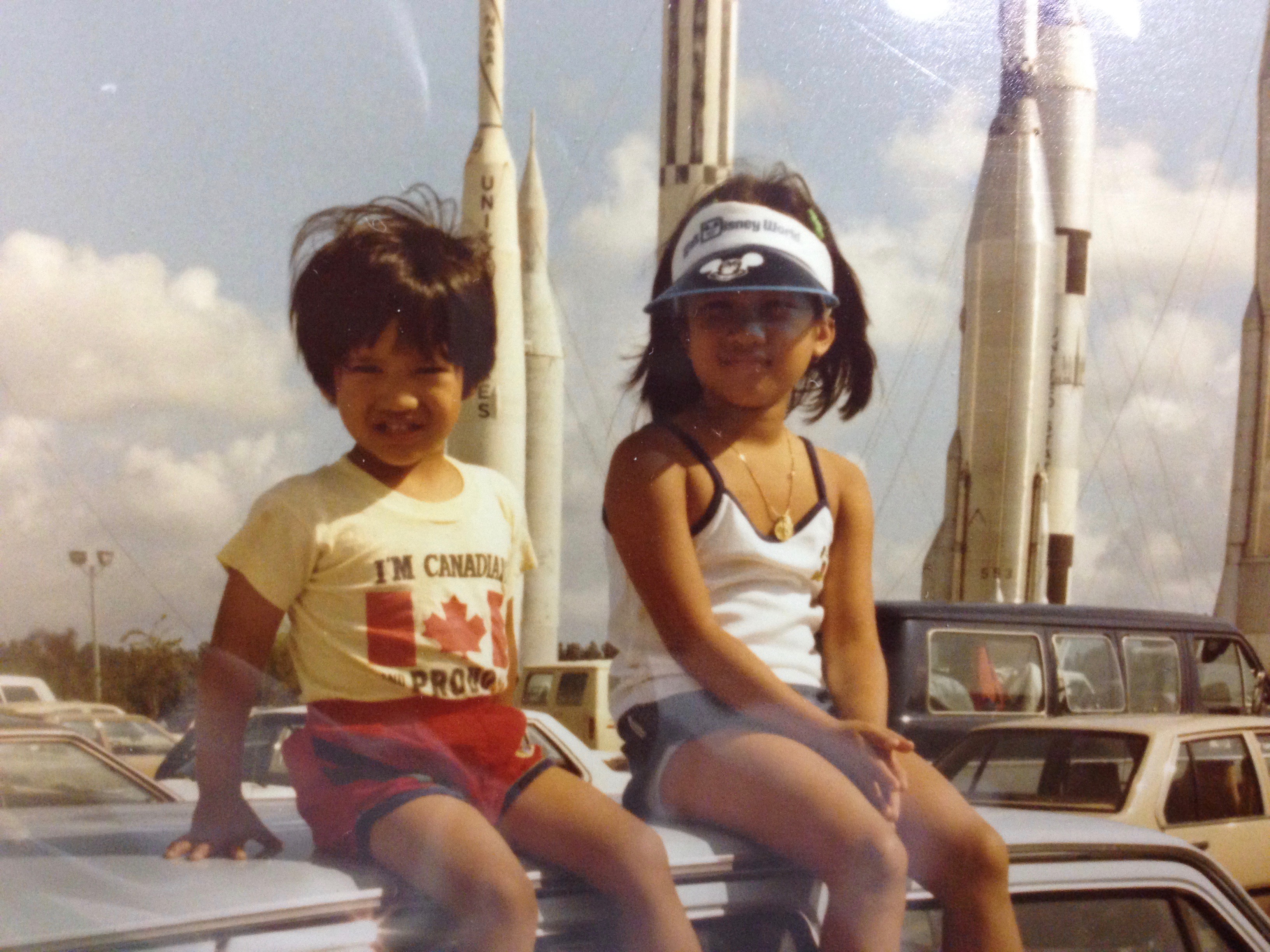 Two young children sit on a car in front of rocket ships